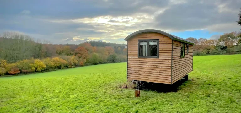 Shepherd hut off-grid in the top of a green field with trees in the distance