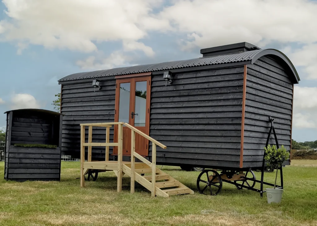 The Grand hut with black wood shiplap exterior and wooden steps to the entrance by Belringham Shepherd Huts Cover